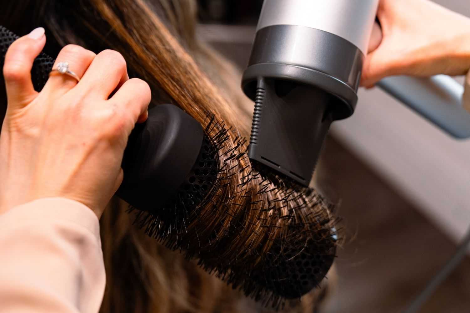 Hair being styled with a round brush and a blow dryer in a salon setting.